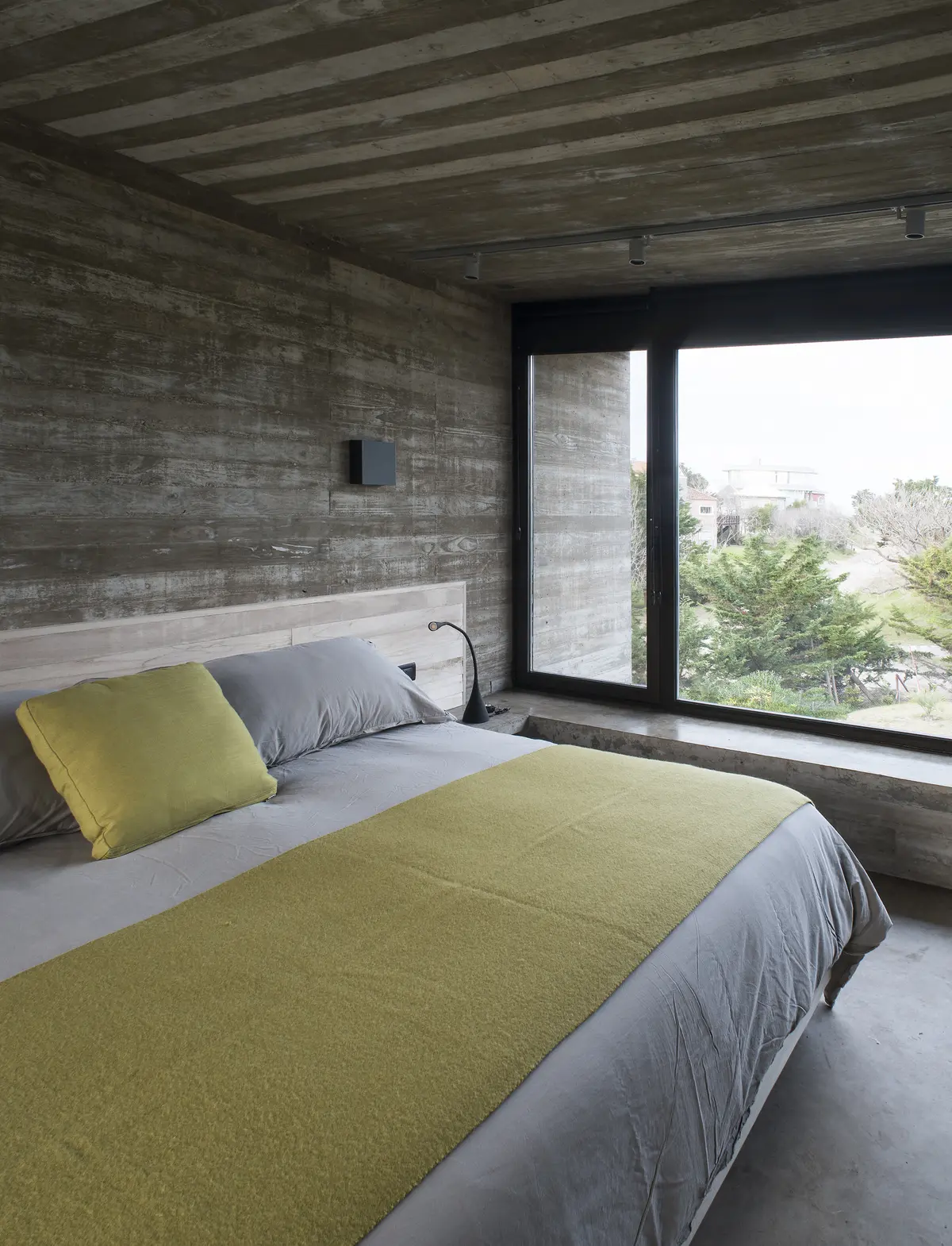 Dormitorio minimalista con hormigón visto y ventanal panorámico — proyecto Casa Cariló, por Luciano Kruk, en Cariló