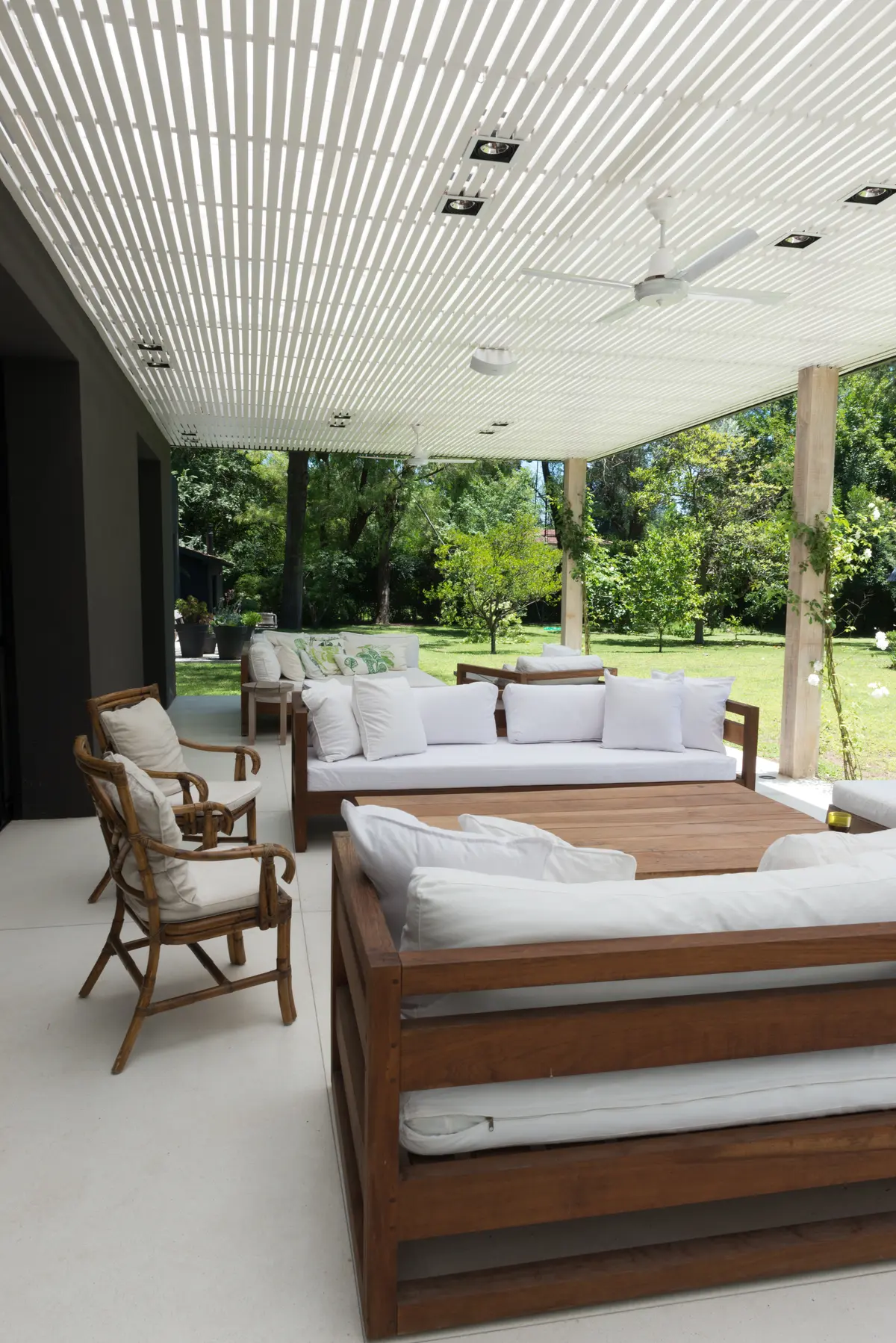 Pátio moderno com teto de ripas, móveis de madeira e vime, cercado por vegetação — projeto Casa M, por Estudio Dado, em Pilar