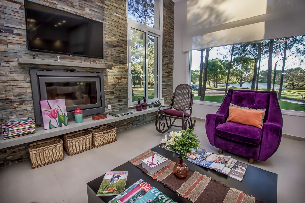 Living moderno con sillón violeta y chimenea de piedra — proyecto Vivienda Unifamiliar en Pinamar, por Estudio Schifano, en Pinamar
