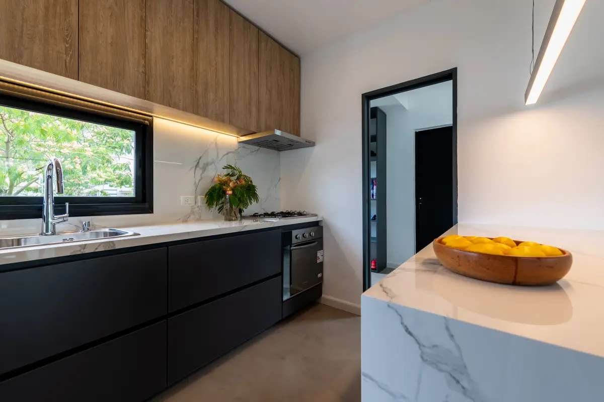 Cocina moderna con muebles de madera y negro, mesada de mármol y luz cálida — proyecto Santa Isabel - Andrea Gonzalez, por ABEJA CONCEPT, en Nordelta