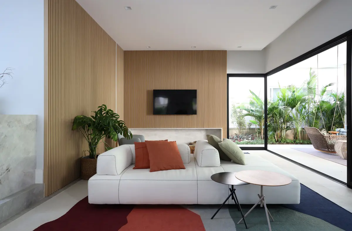 Sala moderna com sofá modular branco e painéis de madeira clara — projeto Projeto Destaque Club&Casa, por Barbara Dundes – Arquitetura + Design