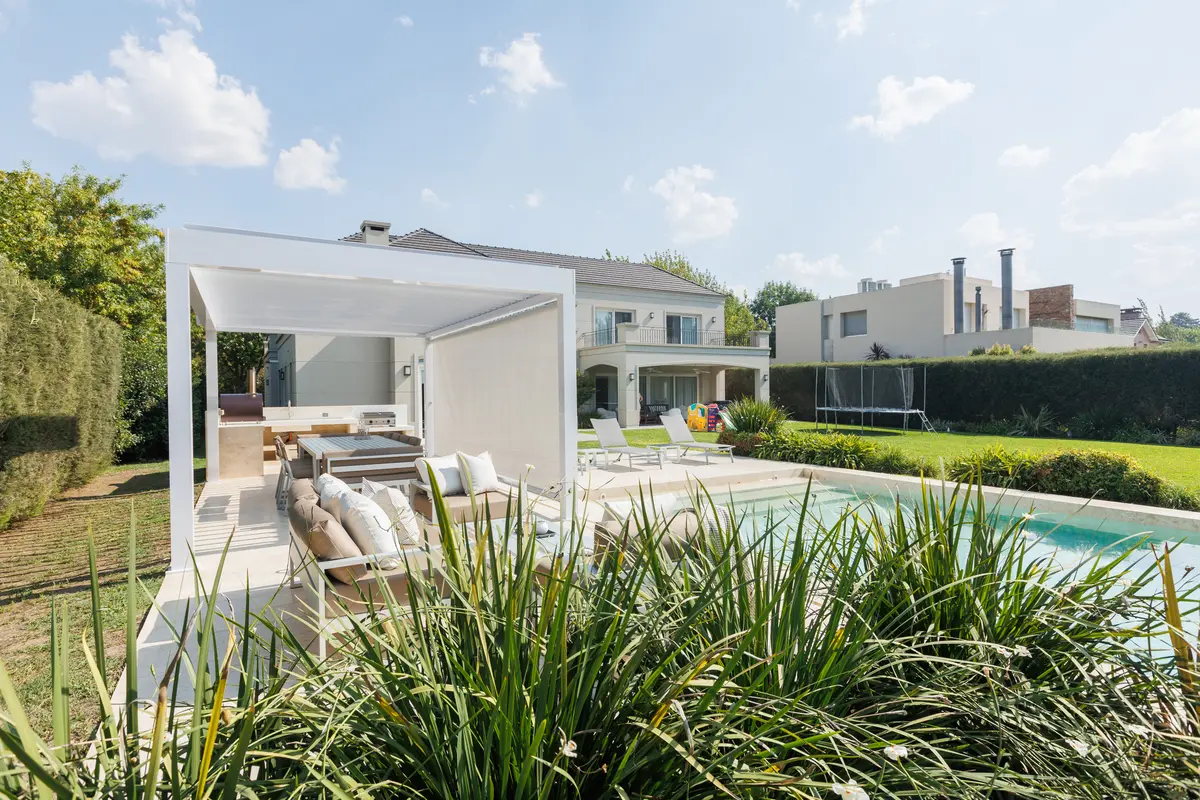 Área de piscina moderna com pergolado, sala de estar externa e vegetação exuberante — projeto TOLDER - PERGOLAS, por Argentina en Obra 2024, em Rincón de Milberg