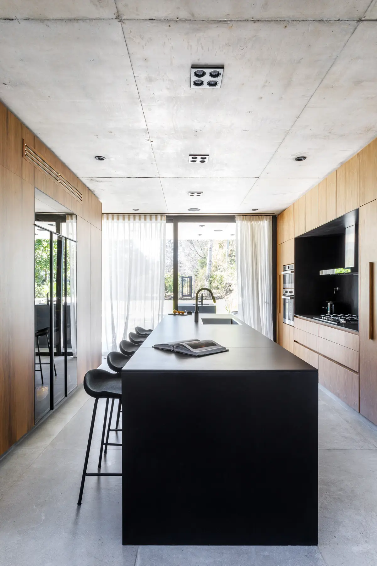Cozinha moderna com ilha preta, teto de concreto e painéis de madeira — projeto CASA AH, por GMARQ, em Garin