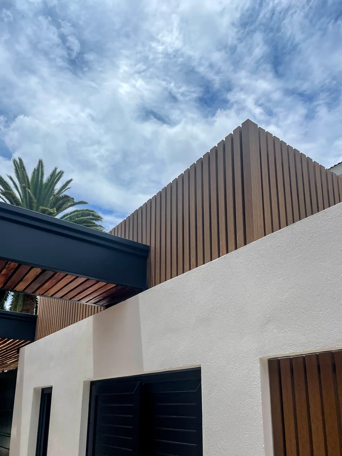 Fachada moderna com revestimento de ripas de madeira e paredes texturizadas brancas — projeto Obra La Posta, por Arq. Lourdes Yarade Saravia, em Pilar