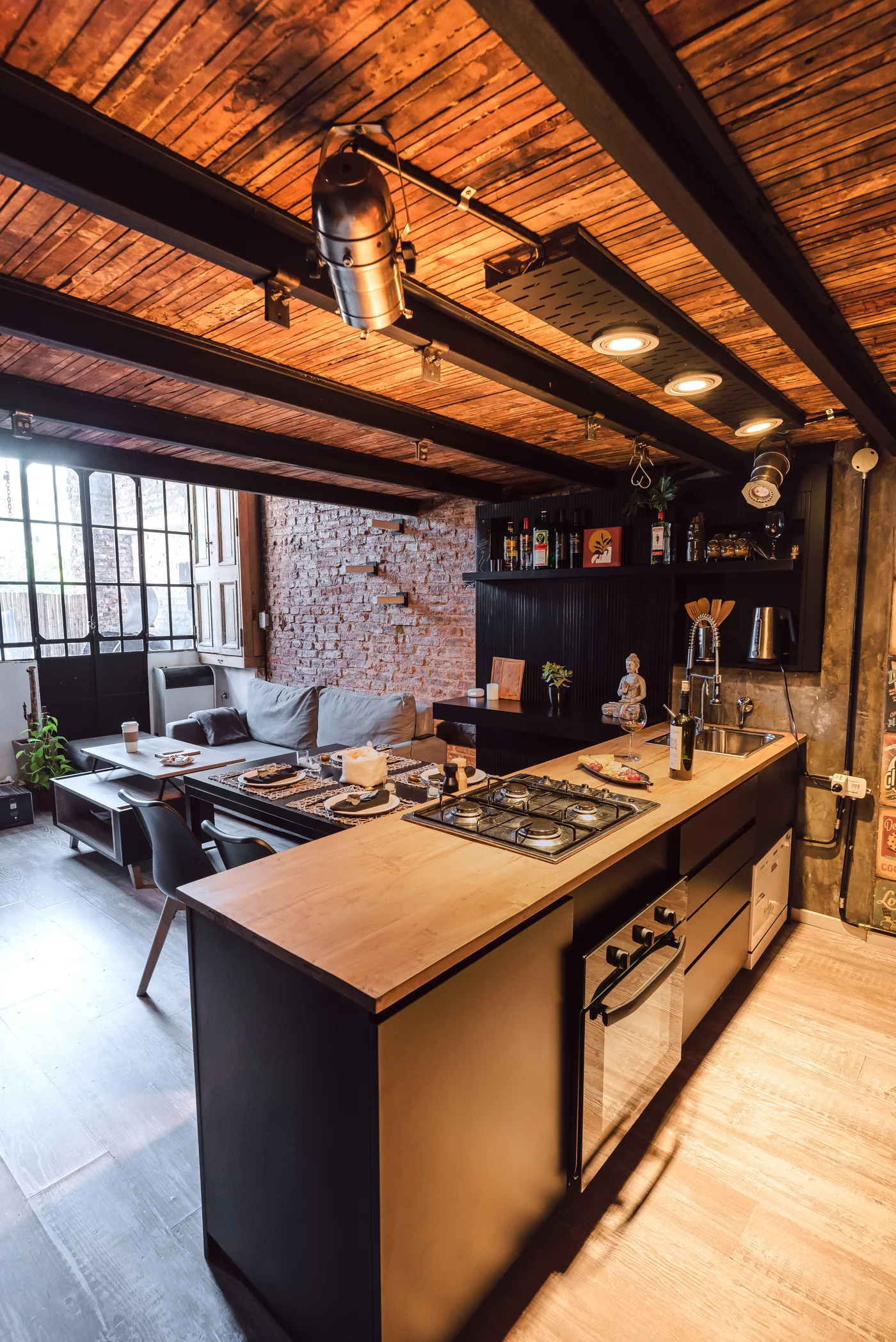 Cocina industrial con isla de madera, techo y vigas expuestas, ladrillo visto.