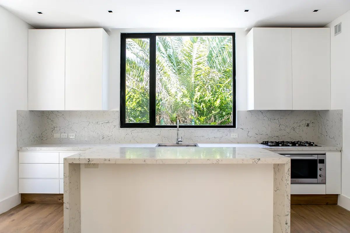 Cocina moderna blanca con isla central y gran ventanal a follaje — proyecto Bosque Chico, por Estudio Arq. María Sioli, en Garin
