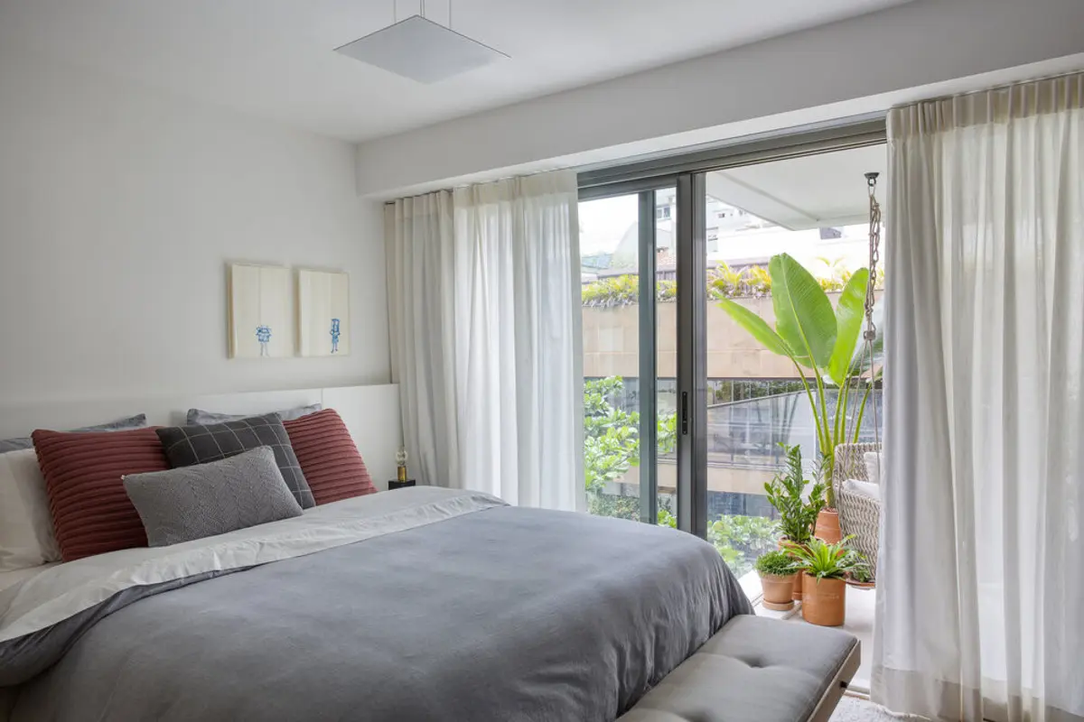 Dormitorio luminoso con cama gris, cortinas y balcón con vista al jardín — proyecto JG House, por Studio Ro-ca