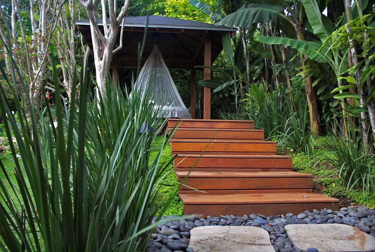 Acceso con deck madera, plantas laterales y estructura moderna al fondo — proyecto Residência JB, por Gil Fialho