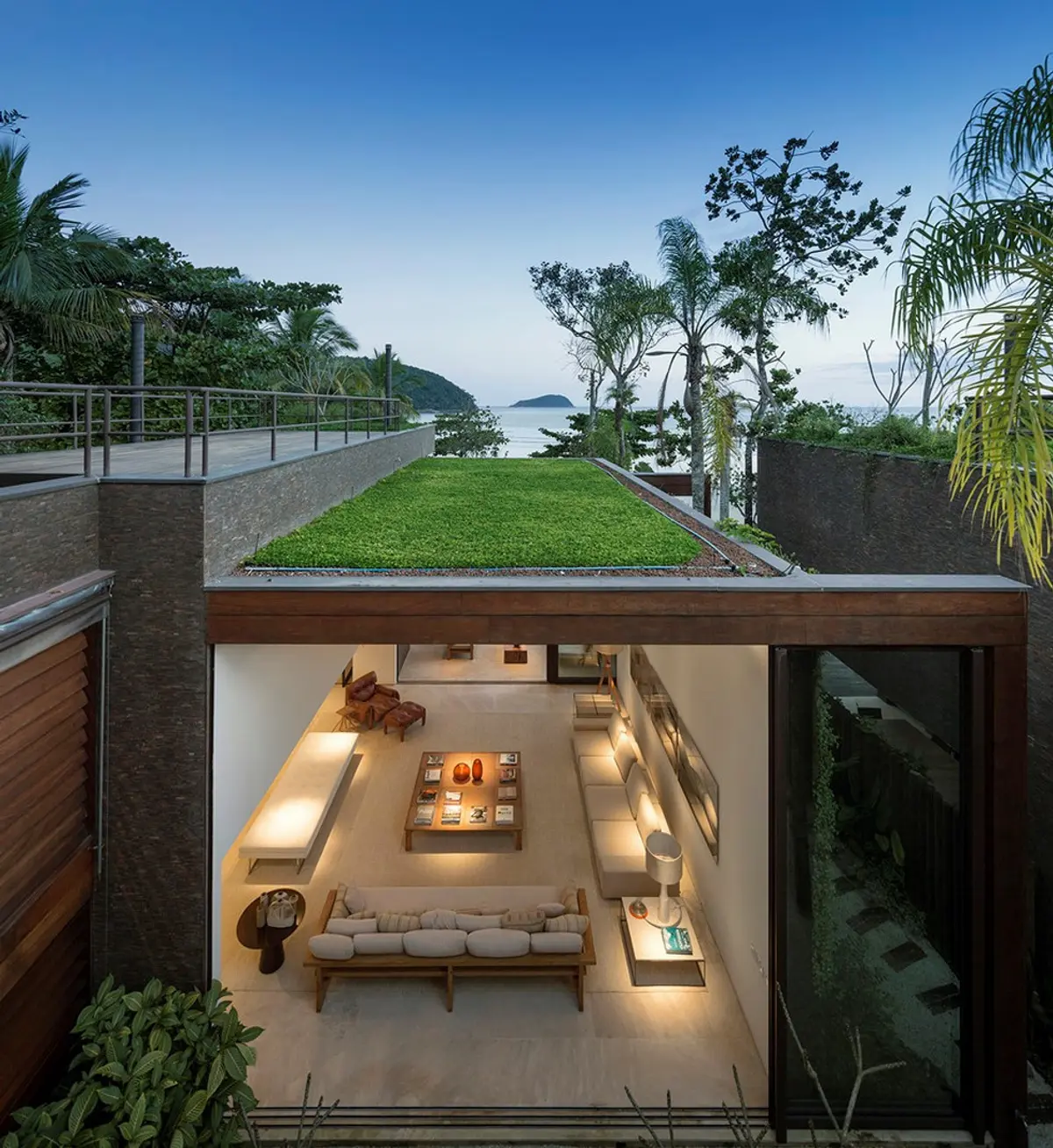 Terraza moderna con piso verde, vista al mar y living subterráneo — proyecto West Whales, por Gil Fialho