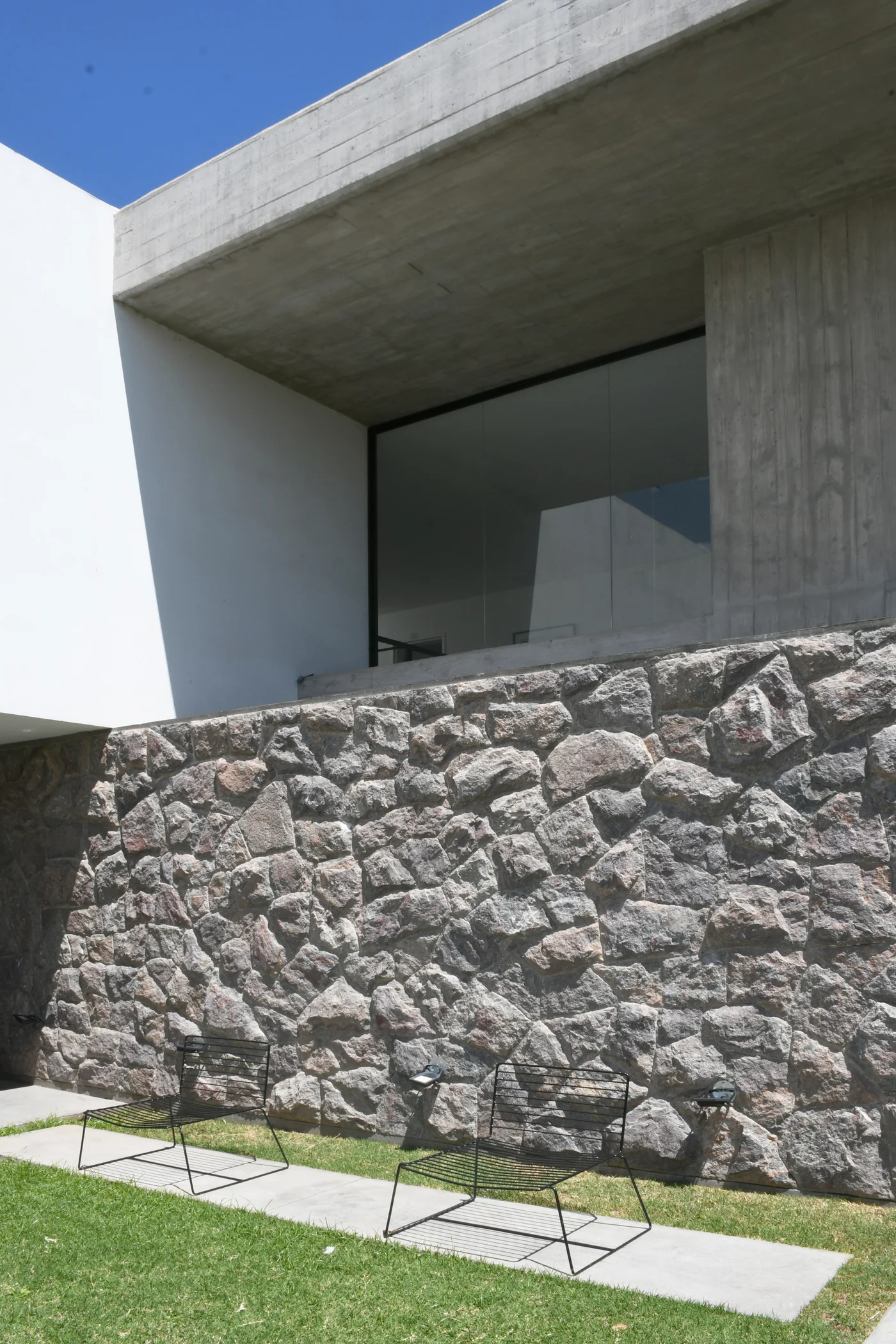 Fachada contemporánea con muro piedra, voladizo hormigón y ventanal
