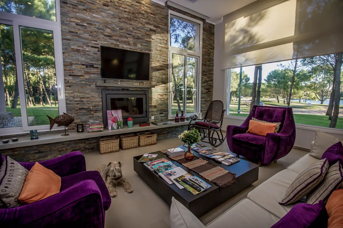 Living moderno con chimenea de piedra y sillones violetas vibrantes — proyecto Vivienda Unifamiliar en Pinamar, por Estudio Schifano, en Pinamar