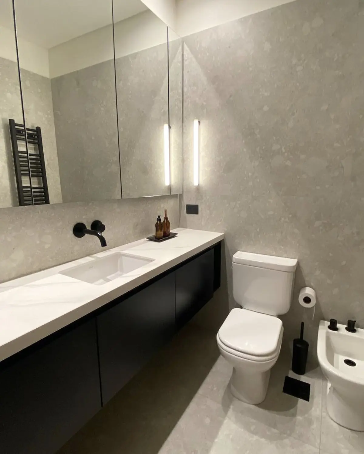 Banheiro moderno cinza com mármore, madeira preta, pia integrada e torneira de parede — projeto Baños Belgrano, por Cudini Estudio, em Belgrano