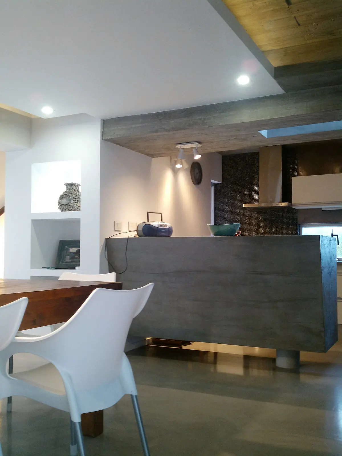 Cozinha moderna com ilha de concreto e cadeiras contemporâneas — projeto VILLA ESMERALDA, por GJF estudio, em Pinamar