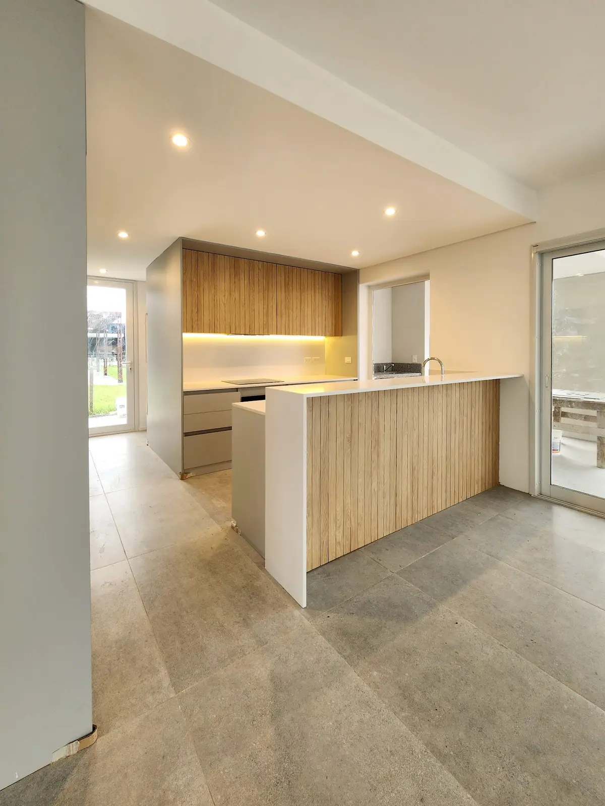 Cozinha moderna com ilha de ripas de madeira e bancada branca — projeto Acacias 265, por BARBALACO ARQUITECTOS, em Belén de Escobar