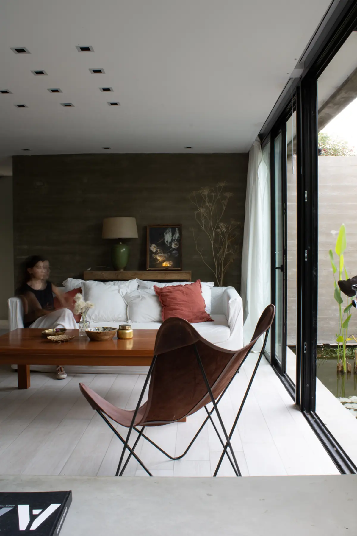 Living moderno con sillón butterfly y pared texturizada oscura — proyecto ampliacion NJ, por arquitectura.JD, en City Bell