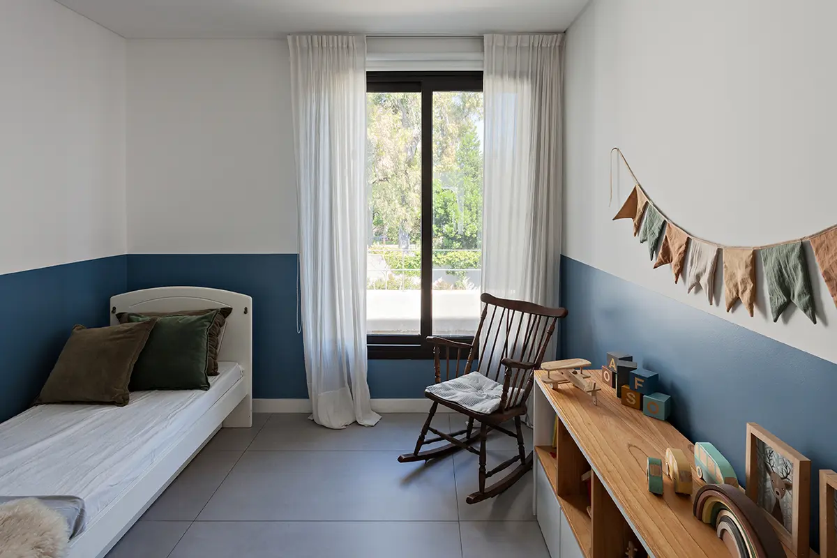 Quarto infantil moderno com parede azul e branca, cama baixa e cadeira de balanço — projeto CASA RDV, por Rastro Estudio, em San Isidro
