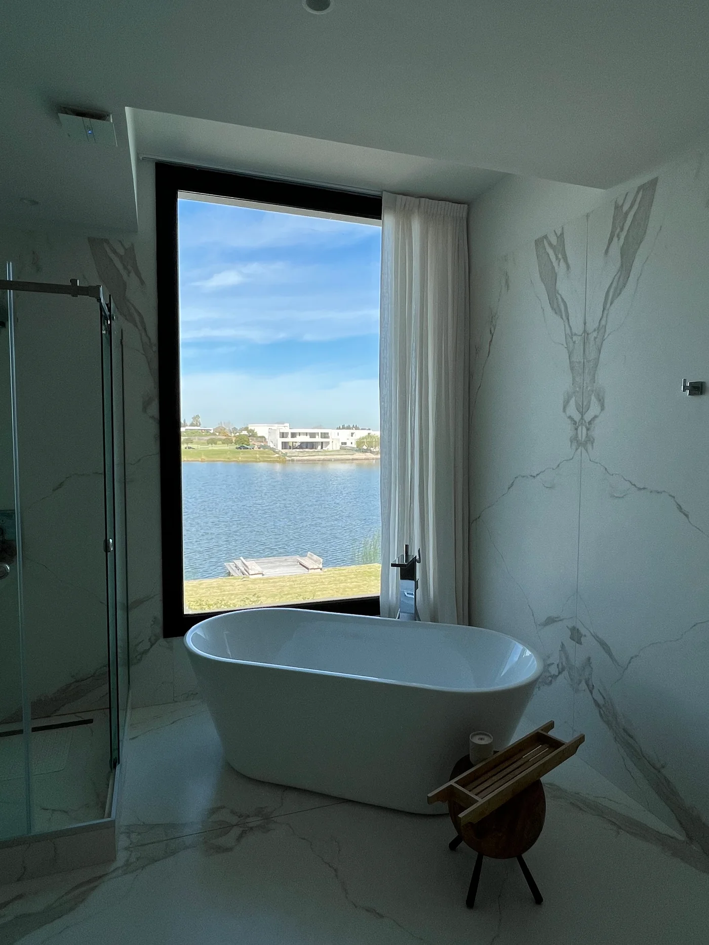 Baño moderno con bañera blanca frente a ventanal con vista al lago