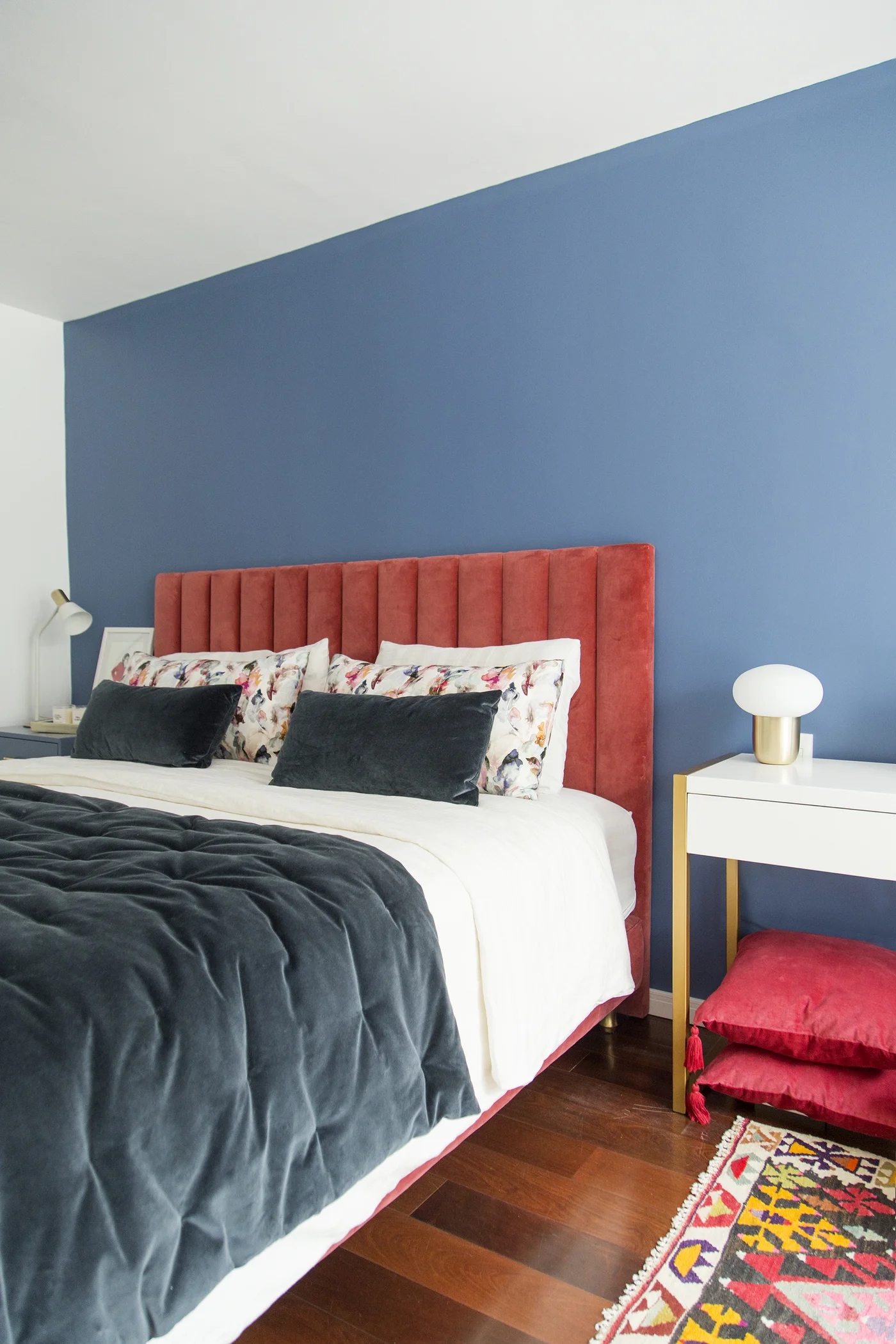 Dormitorio moderno con cama azul, pared destacada y alfombra geométrica.
