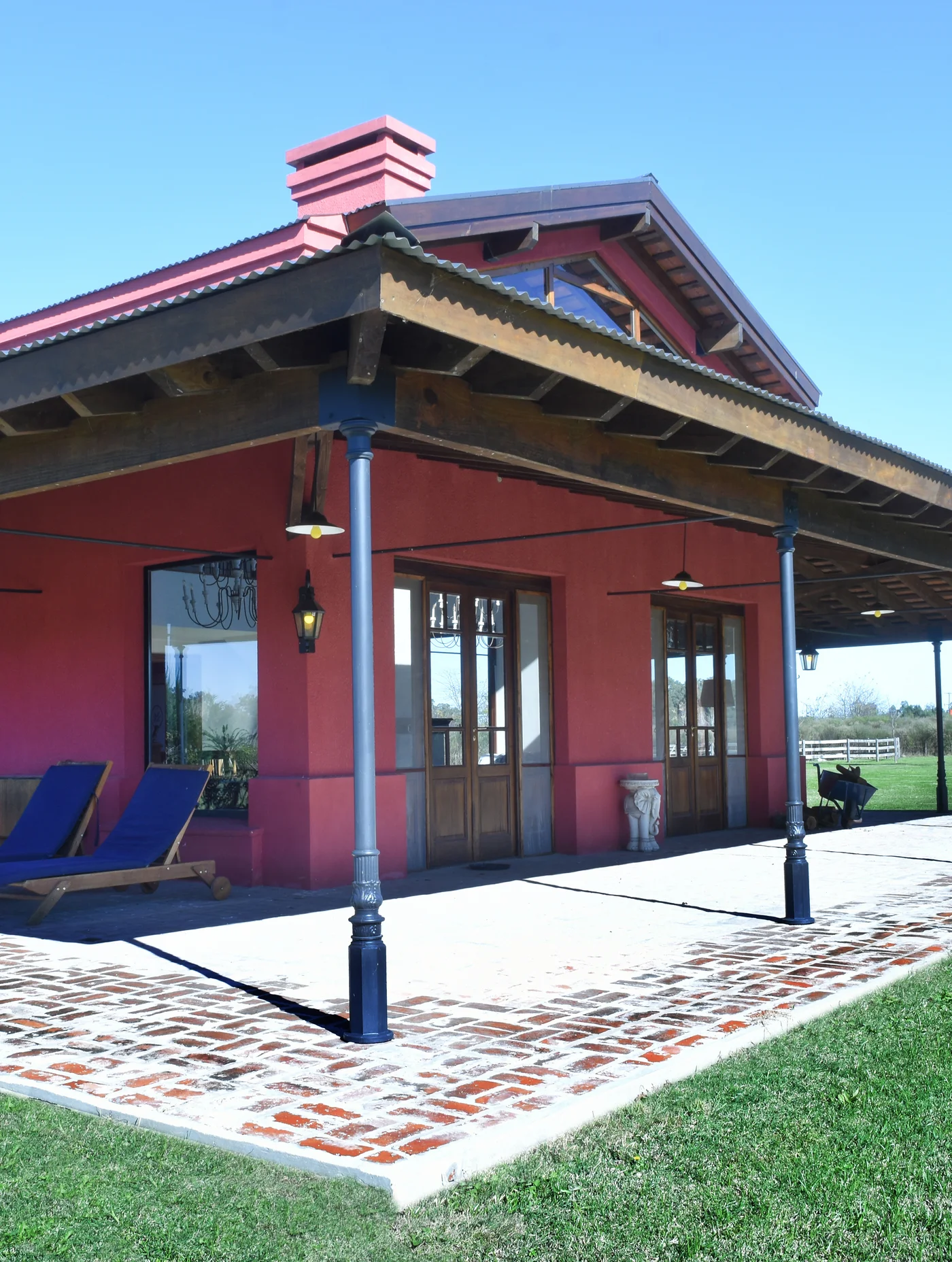 Quincho rural con fachada bordo, columnas azules y piso de ladrillo.