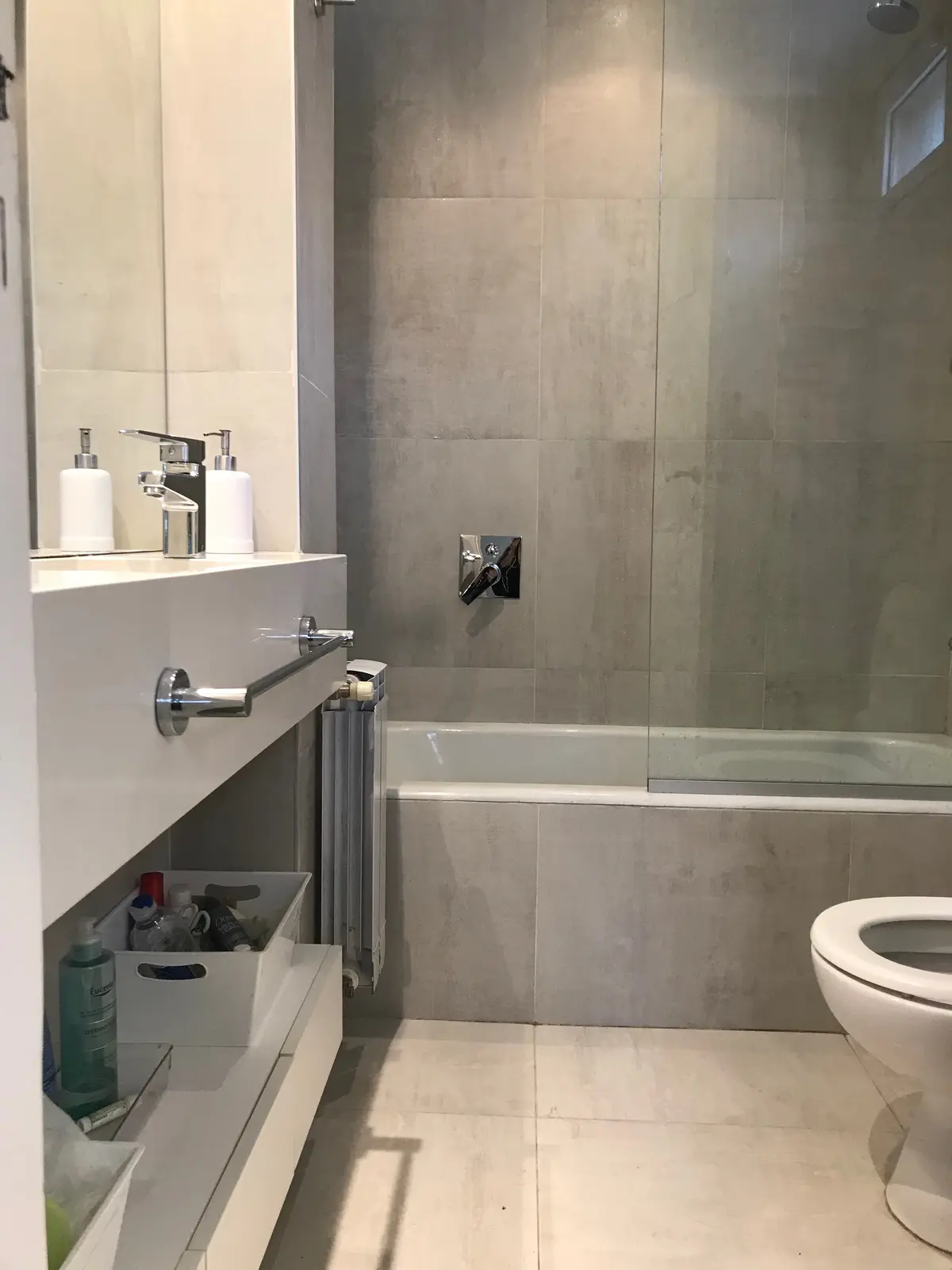 Bano moderno con mampara vidrio, vanitory blanco y piso microcemento gris — proyecto Casa en Martinez, por Rioja Arquitectura, en Martínez