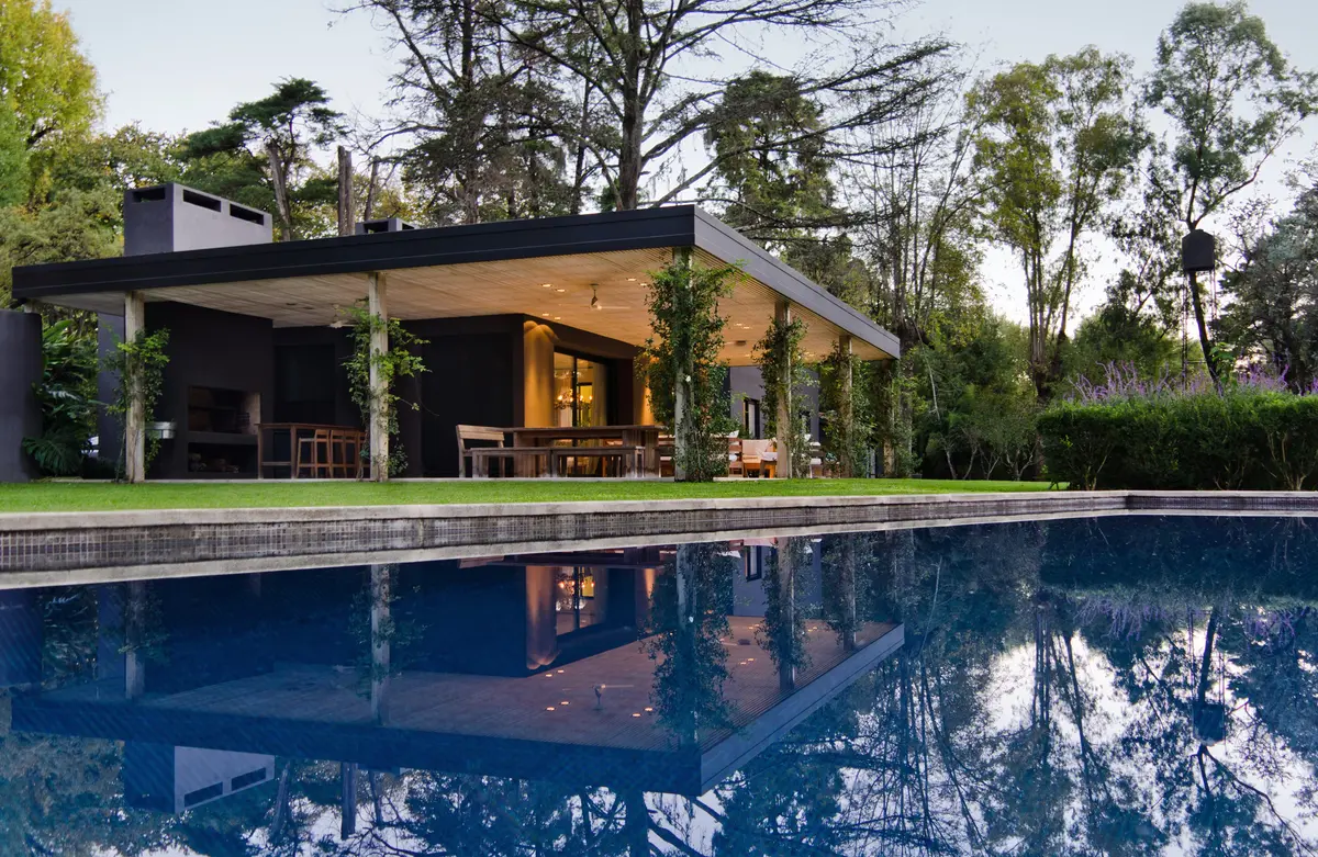 Amplia vista de piscina moderna con techo voladizo y madera — proyecto Casa M, por Estudio Dado, en Pilar