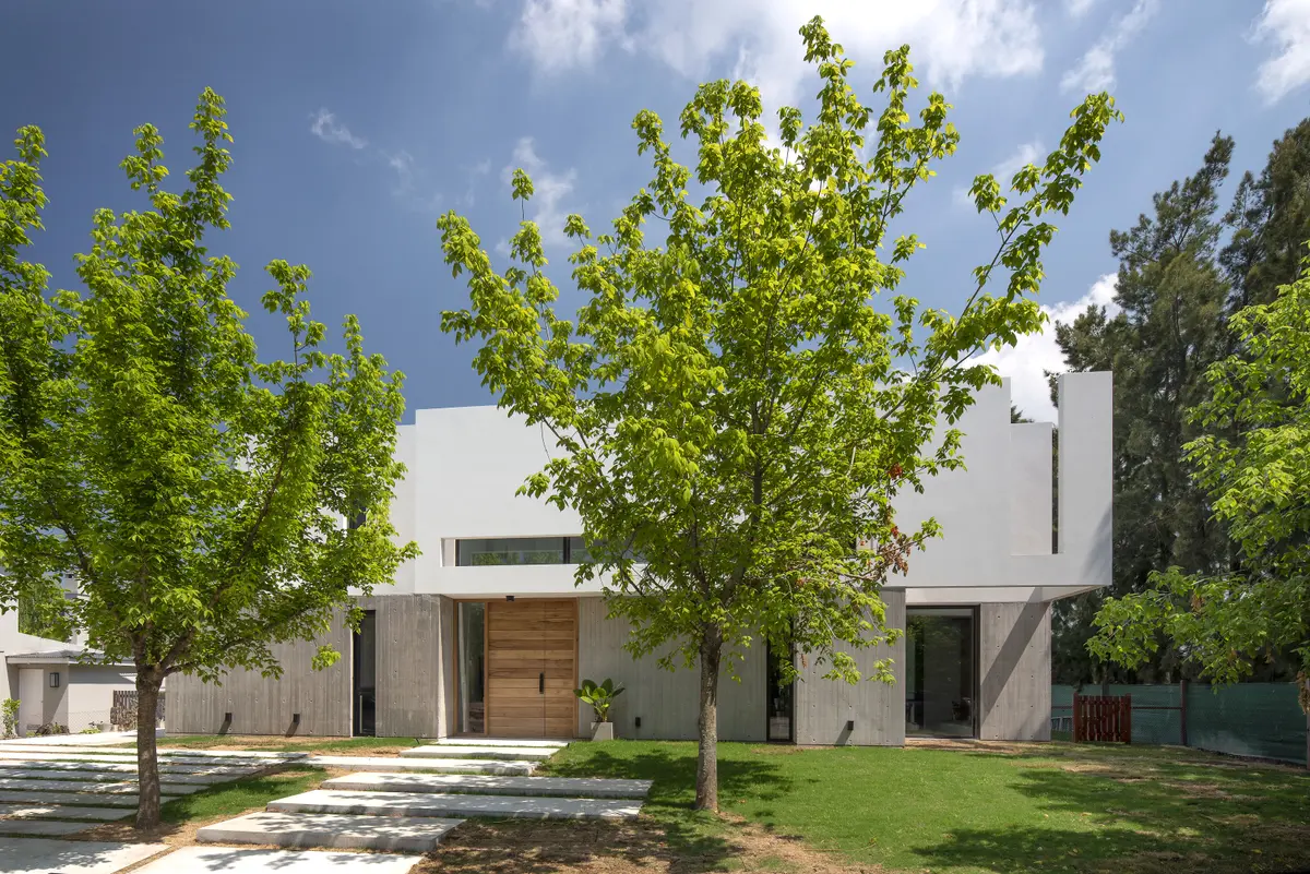 fachada moderna blanca y hormigón con ventanales y mucha vegetación — proyecto Casa PVTM, por Estudio Lak, en Barrio Laguna del Sol