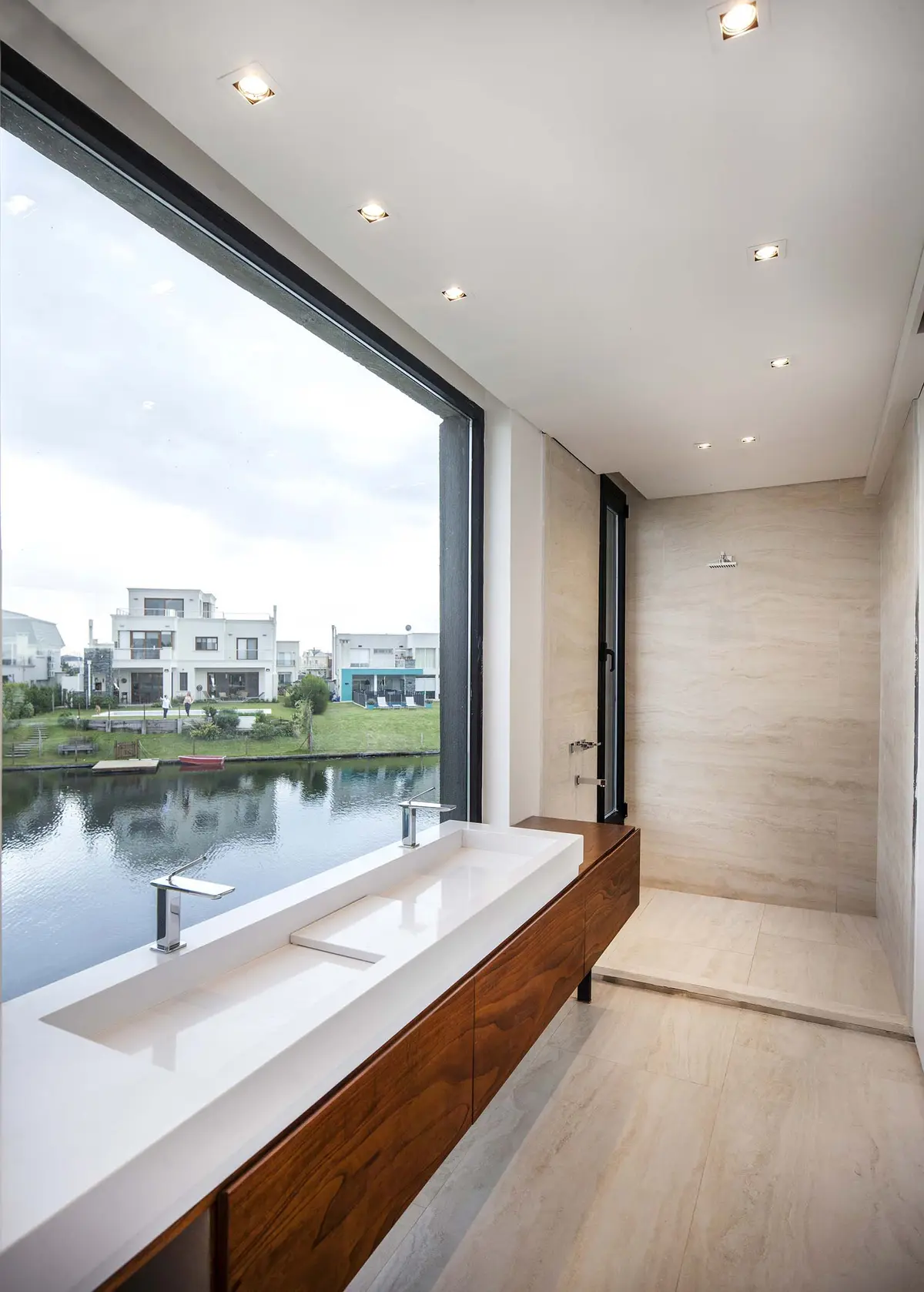 Banheiro moderno com vista para lago, pia dupla e gabinete de madeira — projeto Alisos, por Remy Arquitectos, em Nordelta