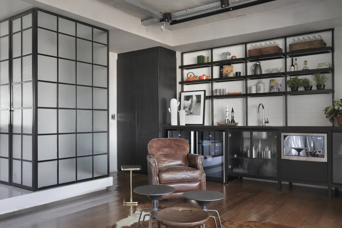 Oficina moderna con estantería negra, sillón cuero y ventanal industrial — proyecto RA Loft, por Studio Ro-ca