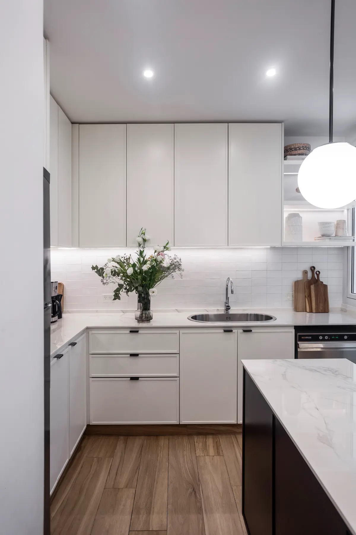Cocina moderna minimalista con isla, gabinetes blancos y luz colgante esférica — proyecto Bustamante, por JT ARQUITECTURA, en Buenos Aires