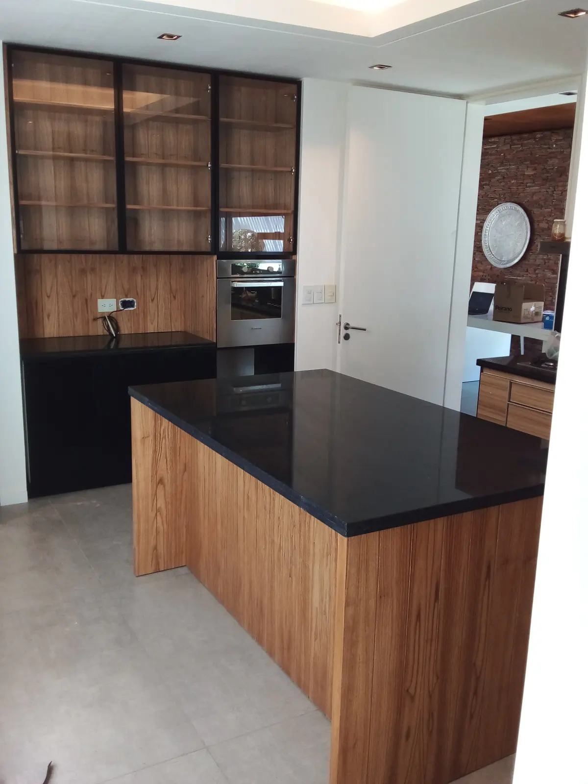 Cocina moderna con isla de madera y mesada negra, gabinetes de vidrio — proyecto cocina en paraiso con detalles negros, por Dnni, en Gonnet