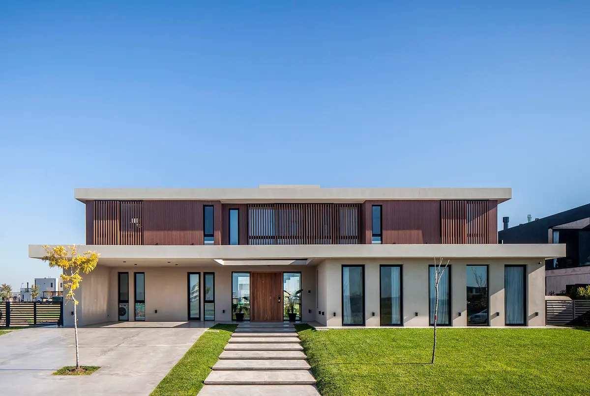 Casa moderna com fachada de madeira e janelas grandes em bairro suburbano — projeto CASA C313, por A'PRIMA - Arquitectura Sustentable, em Provincia de Buenos Aires