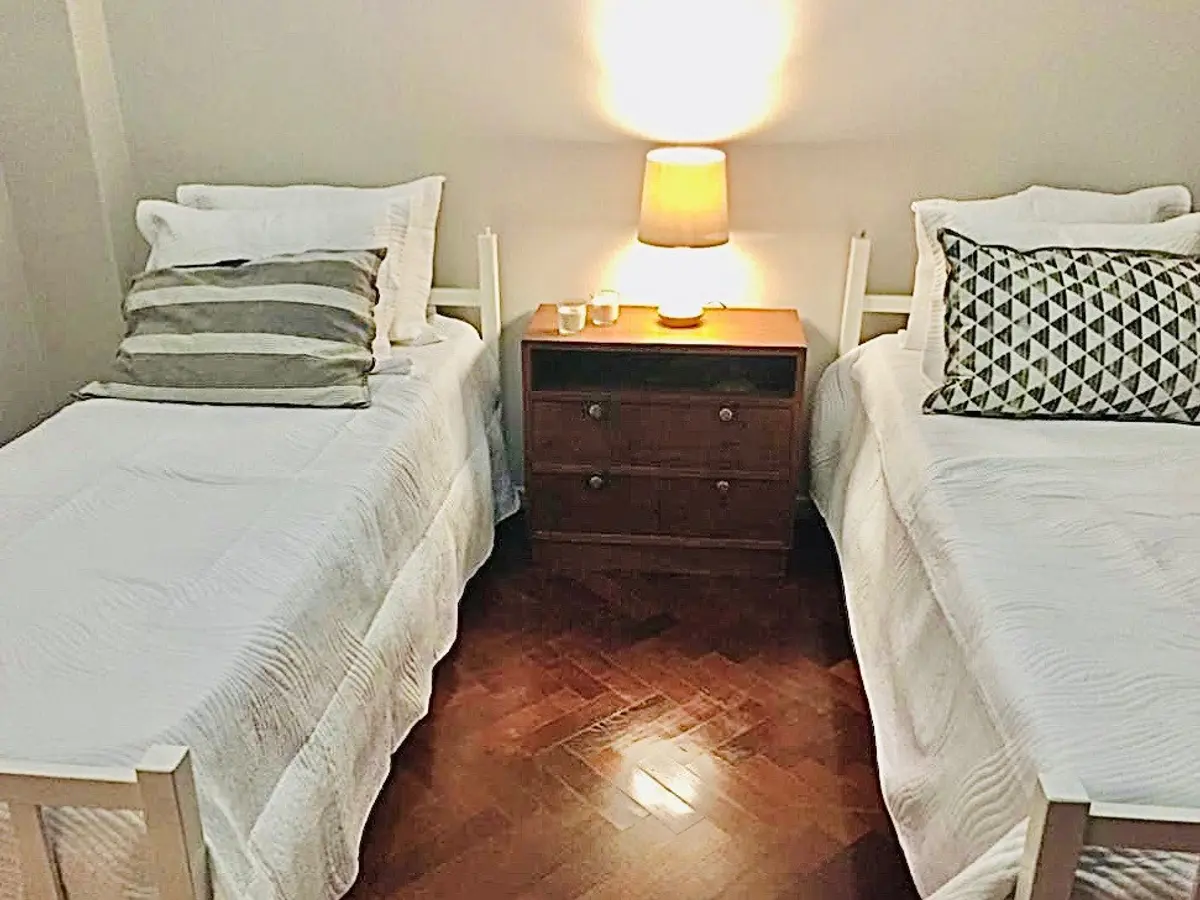 Dormitorio twin con dos camas blancas y piso de madera oscura — proyecto Salguero, por Rioja Arquitectura, en Palermo
