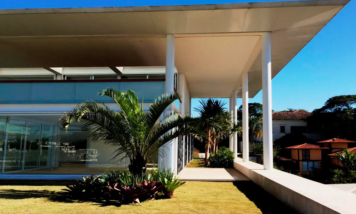 Casa moderna con pergola blanca, jardín y palmeras al atardecer — proyecto Residência HC, por Gil Fialho