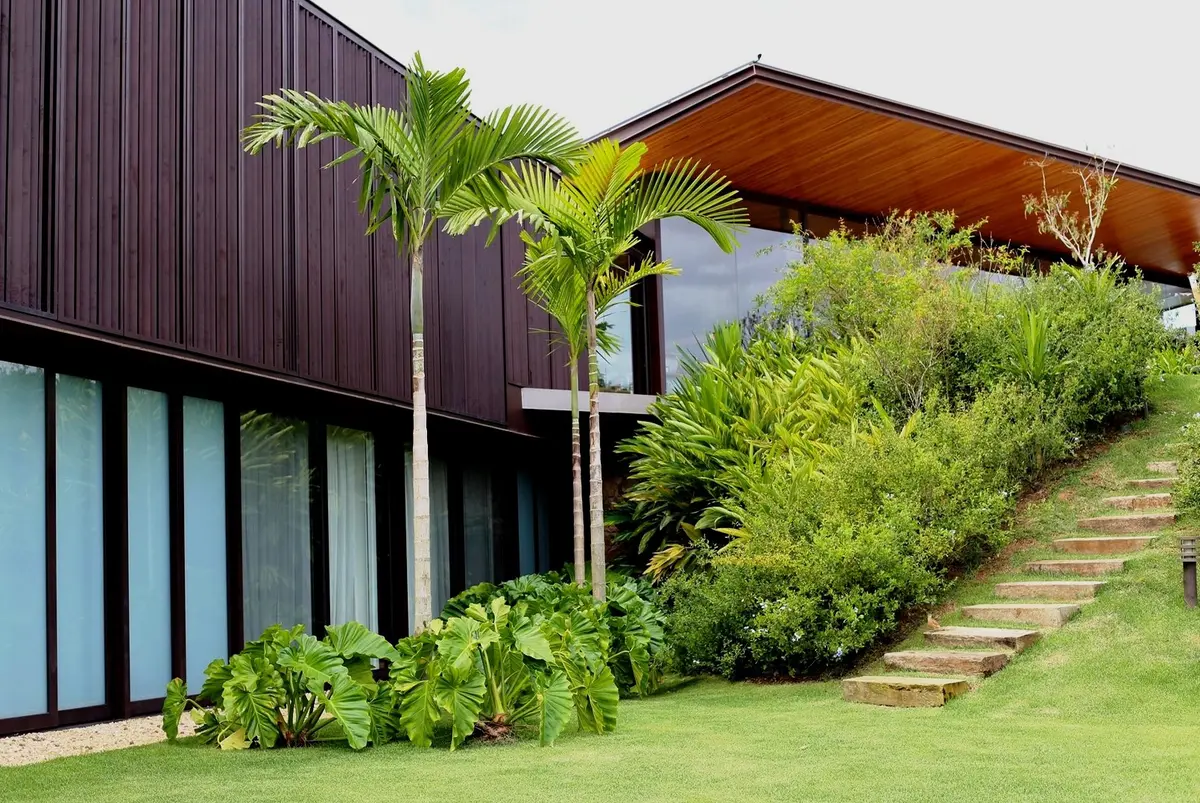 Casa negra moderna con jardín escalonado, palmera y vegetación exuberante — proyecto Residência CA, por Gil Fialho