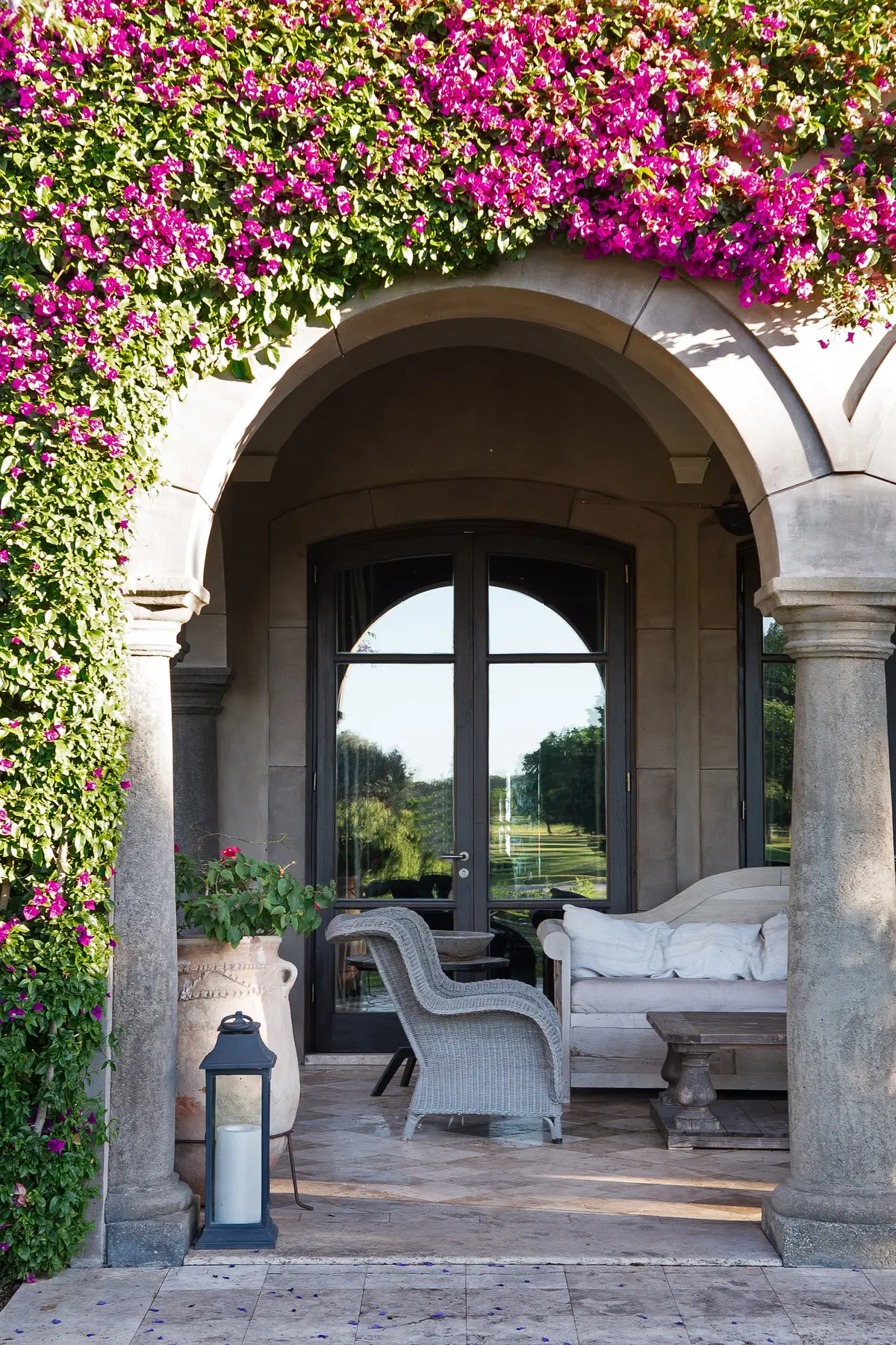 Terraza porticada con arco de piedra y buganvilia magenta — proyecto Casa Toscana , por Estudio Du 