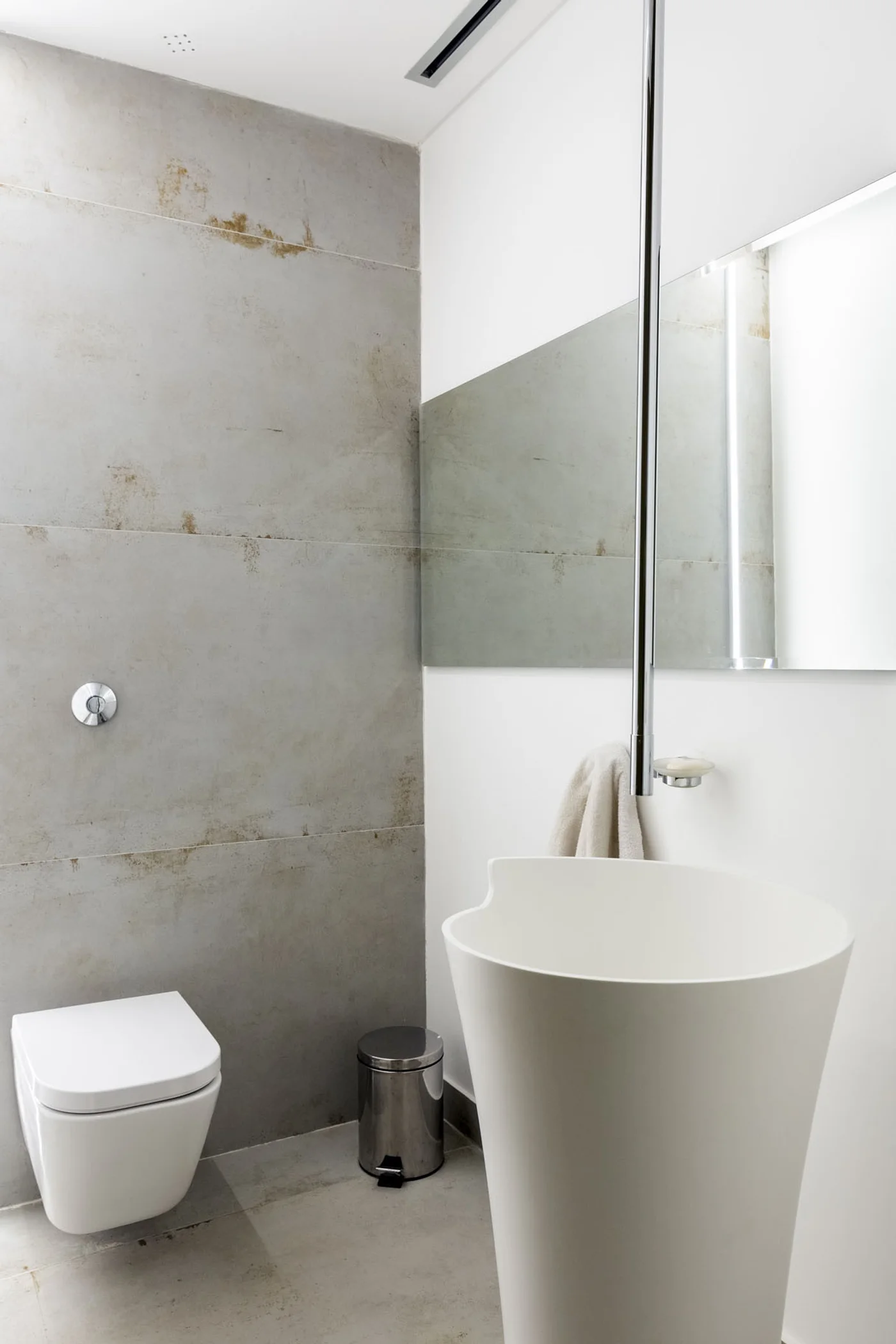 Baño moderno con paredes de hormigón y lavabo pedestal blanco.