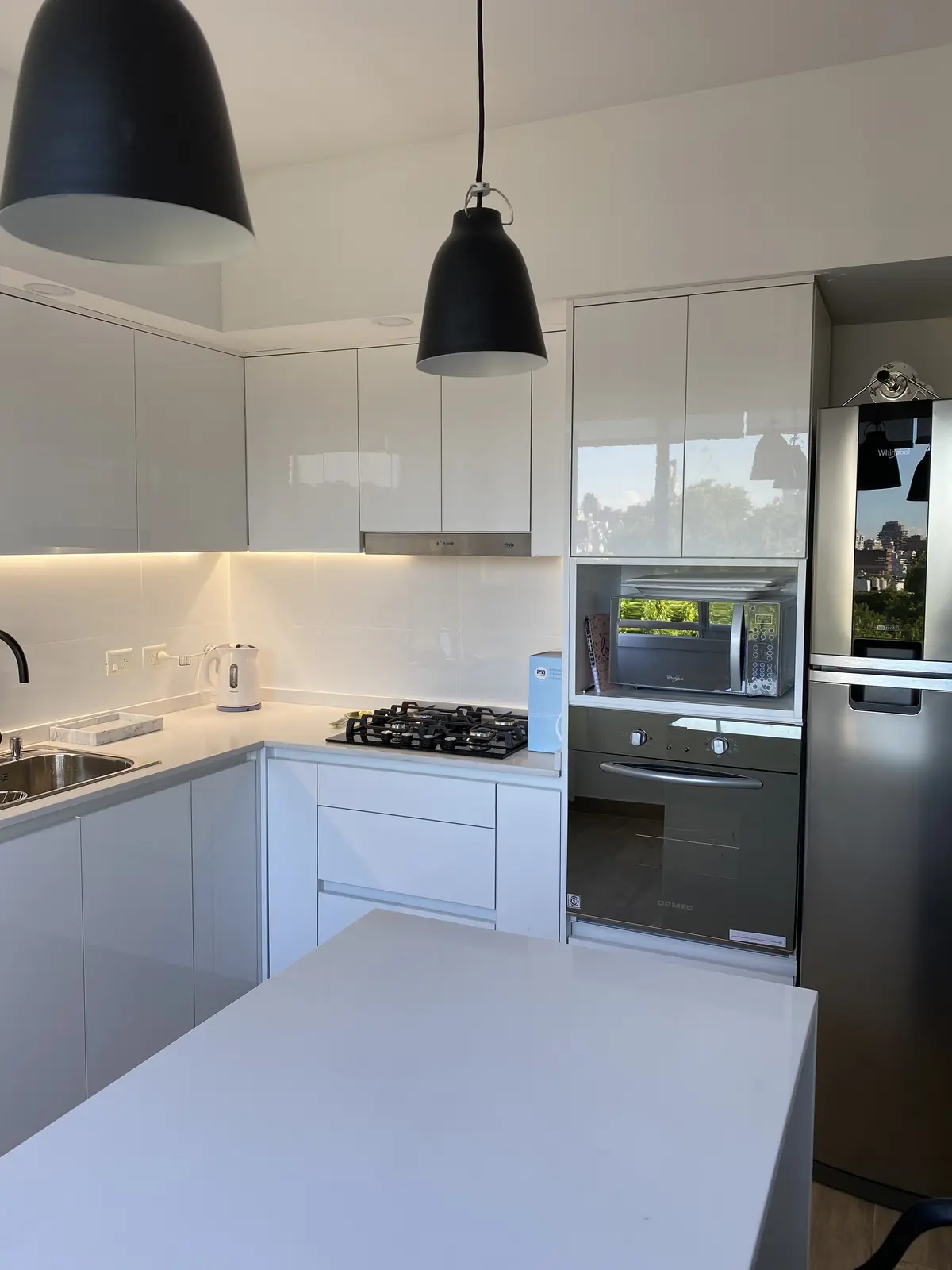 Cocina moderna blanca con isla, muebles lacados y electrodomésticos negros — proyecto DEPTO OH, por Estudio Grupo 32, en Buenos Aires