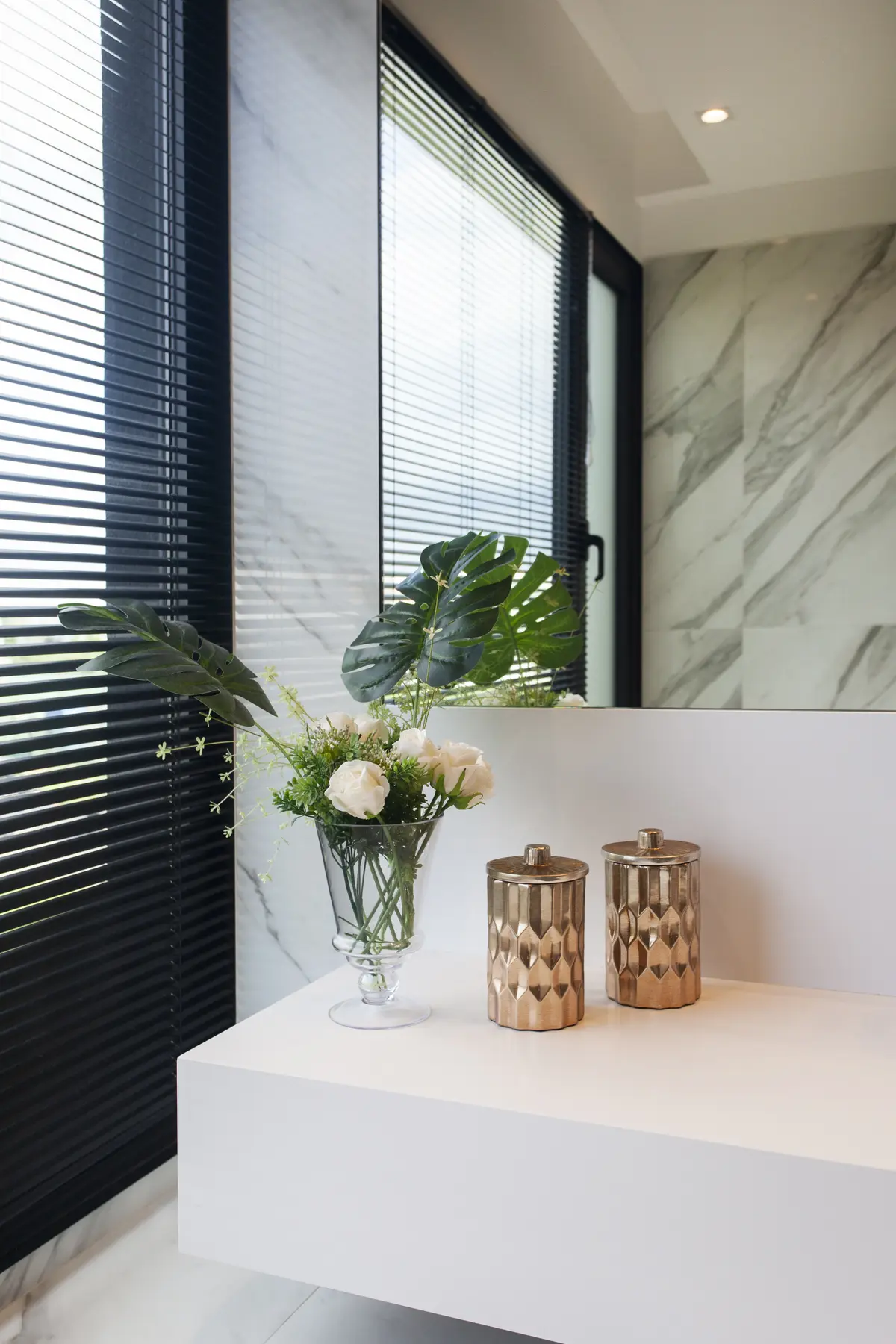 Baño moderno con paredes de mármol, jarrones dorados y flores — proyecto Casa BJM, por Vanguarda Arquitectos, en Belén de Escobar
