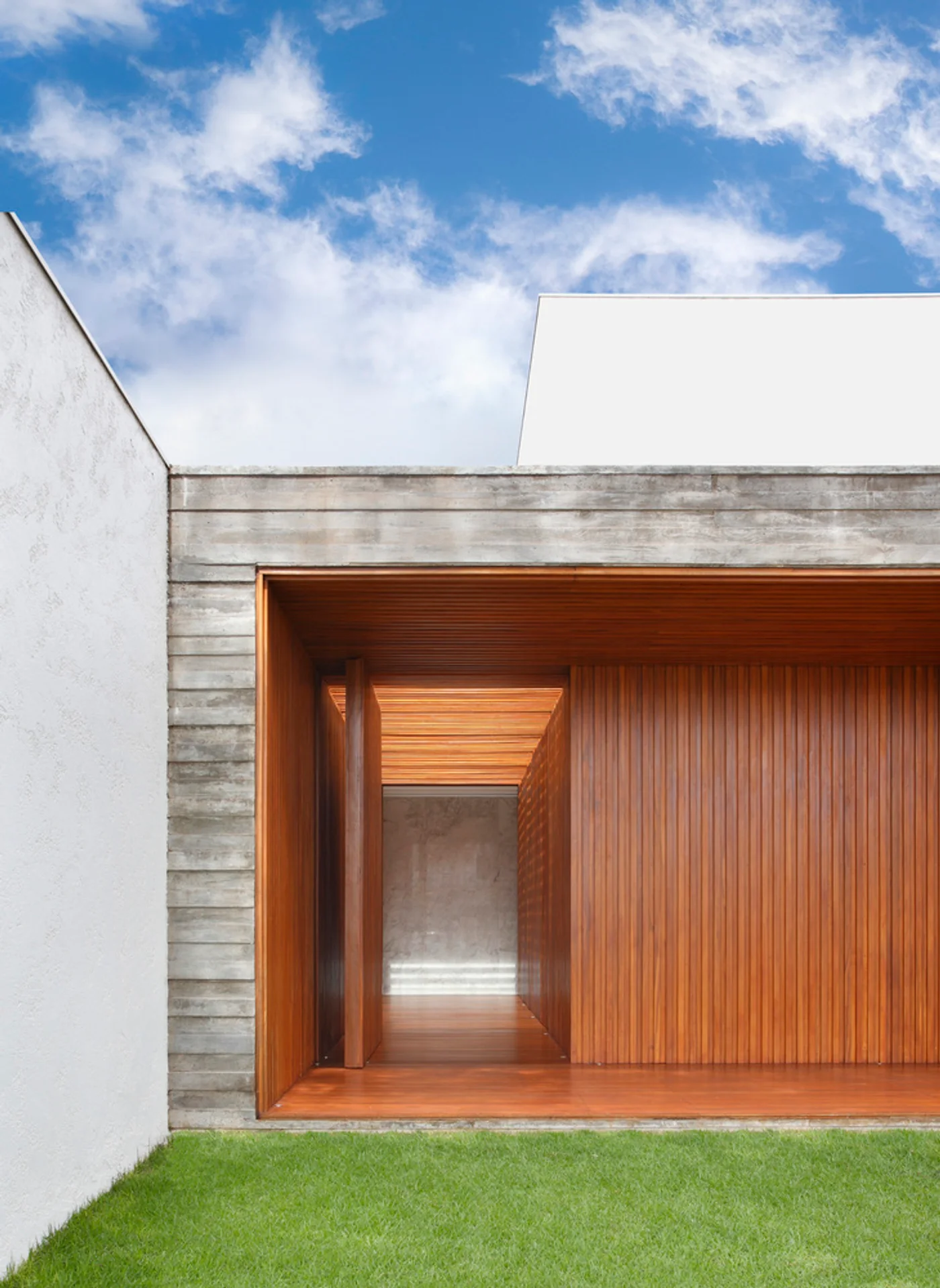 Fachada moderna con hormigón y madera, entrada de madera con listones verticales.