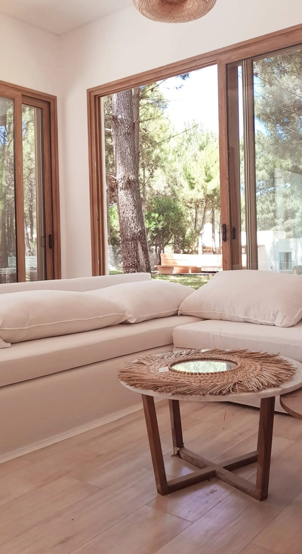 Living moderno con ventanales al bosque y sillones bajos — proyecto Casa NF, por TAVA Coop, en Pinamar
