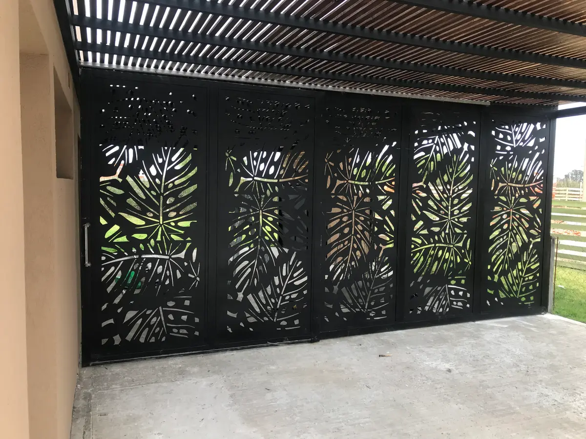 Portão preto vazado com folhas e pérgola de madeira — projeto Chapa calada decorativa, tríptico árbol de la vida oara portones corredizos y ce, por Pintastic, em Belén de Escobar