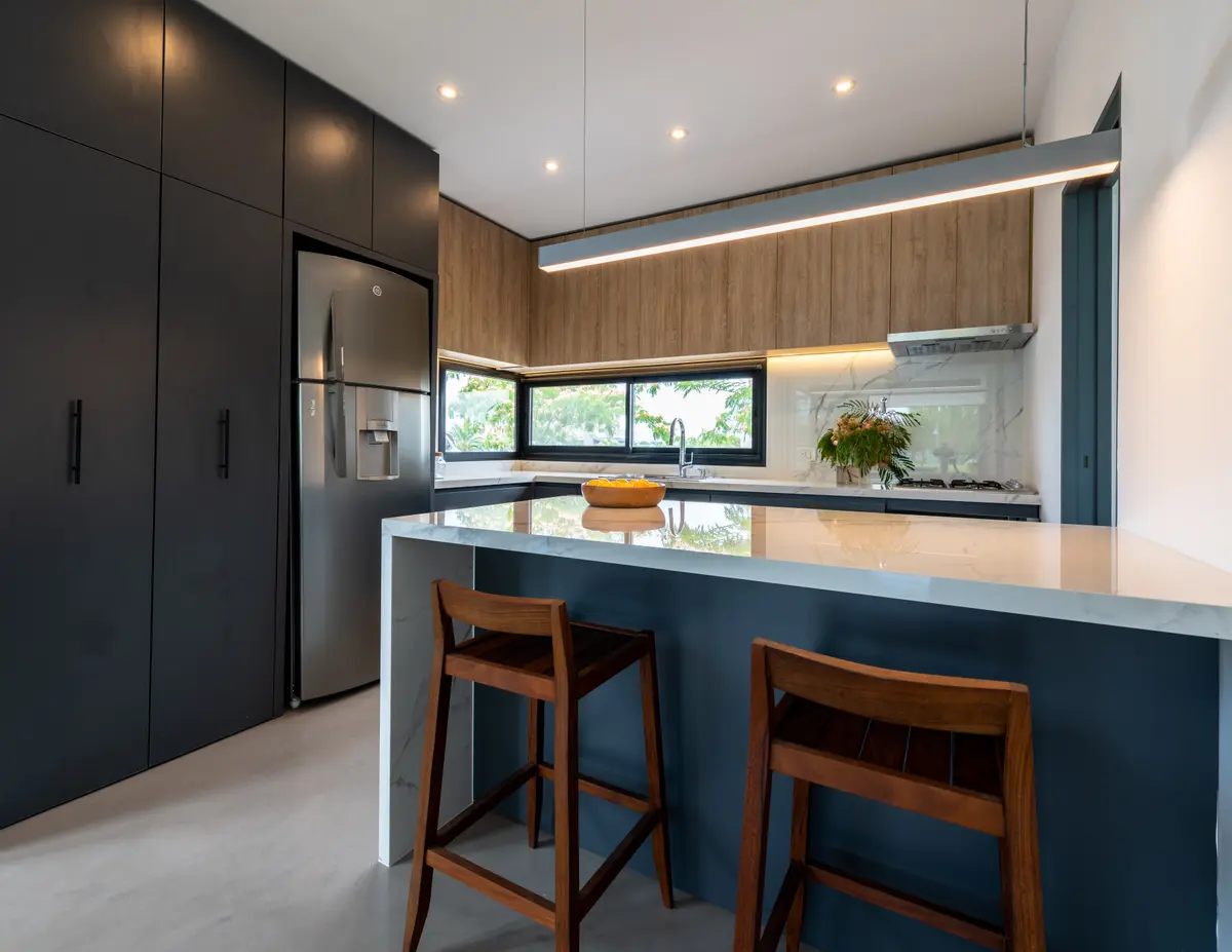 Cozinha moderna com ilha, armários escuros e bancada branca — projeto Santa Isabel - Andrea Gonzalez, por ABEJA CONCEPT, em Nordelta