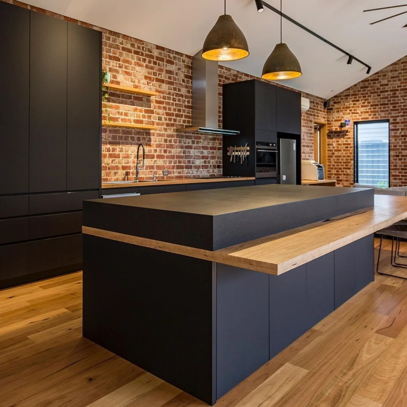 Cocina moderna industrial con pared de ladrillo expuesto y isla negra.