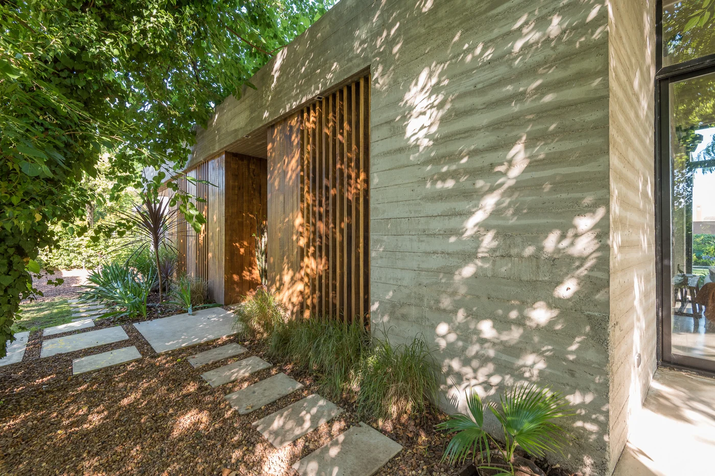 Fachada moderna con hormigón expuesto, entrada de listones de madera y jardín