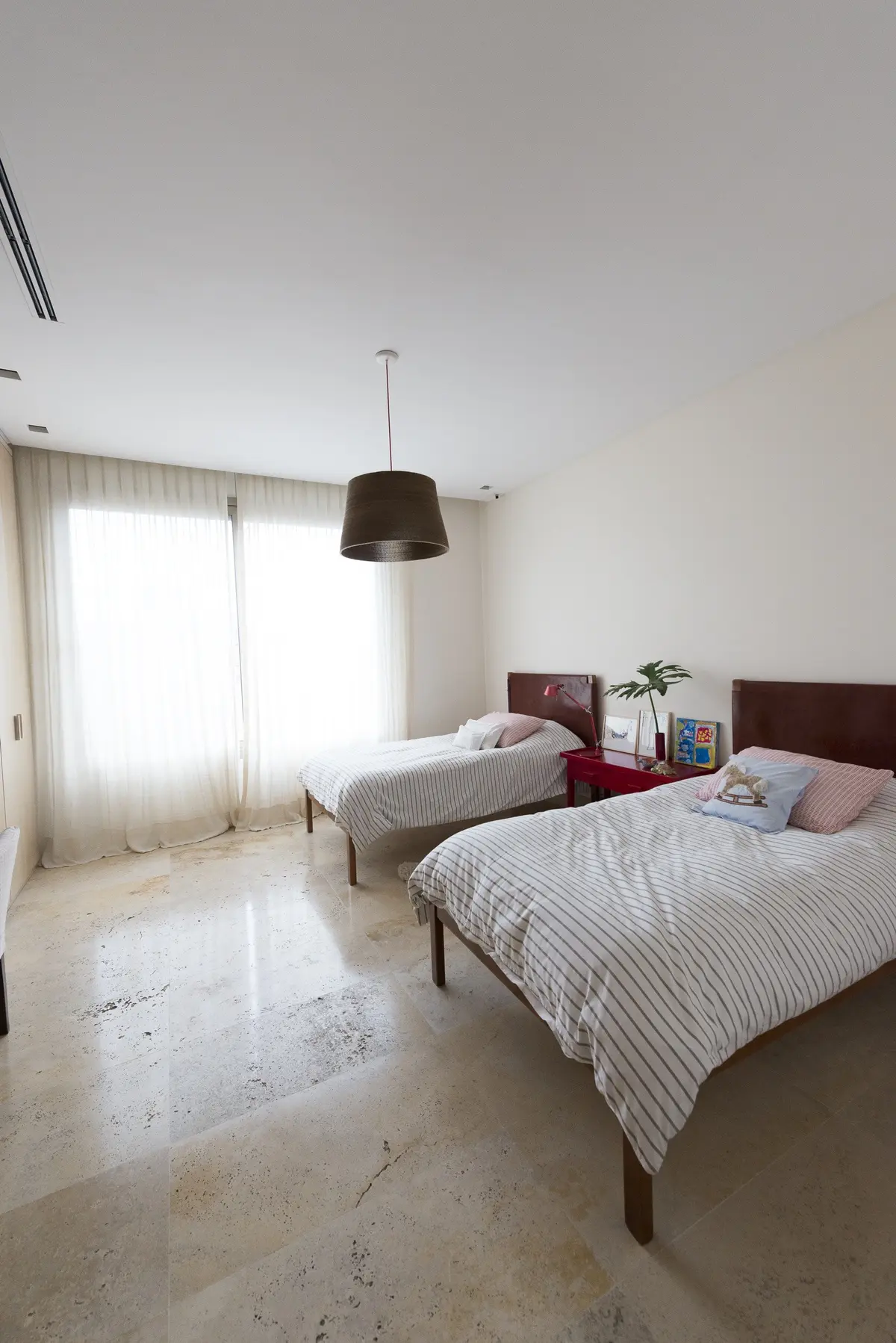 Dormitorio moderno con dos camas, suelo de piedra y grandes ventanales — proyecto Casa H, por Estudio Dado, en Belgrano