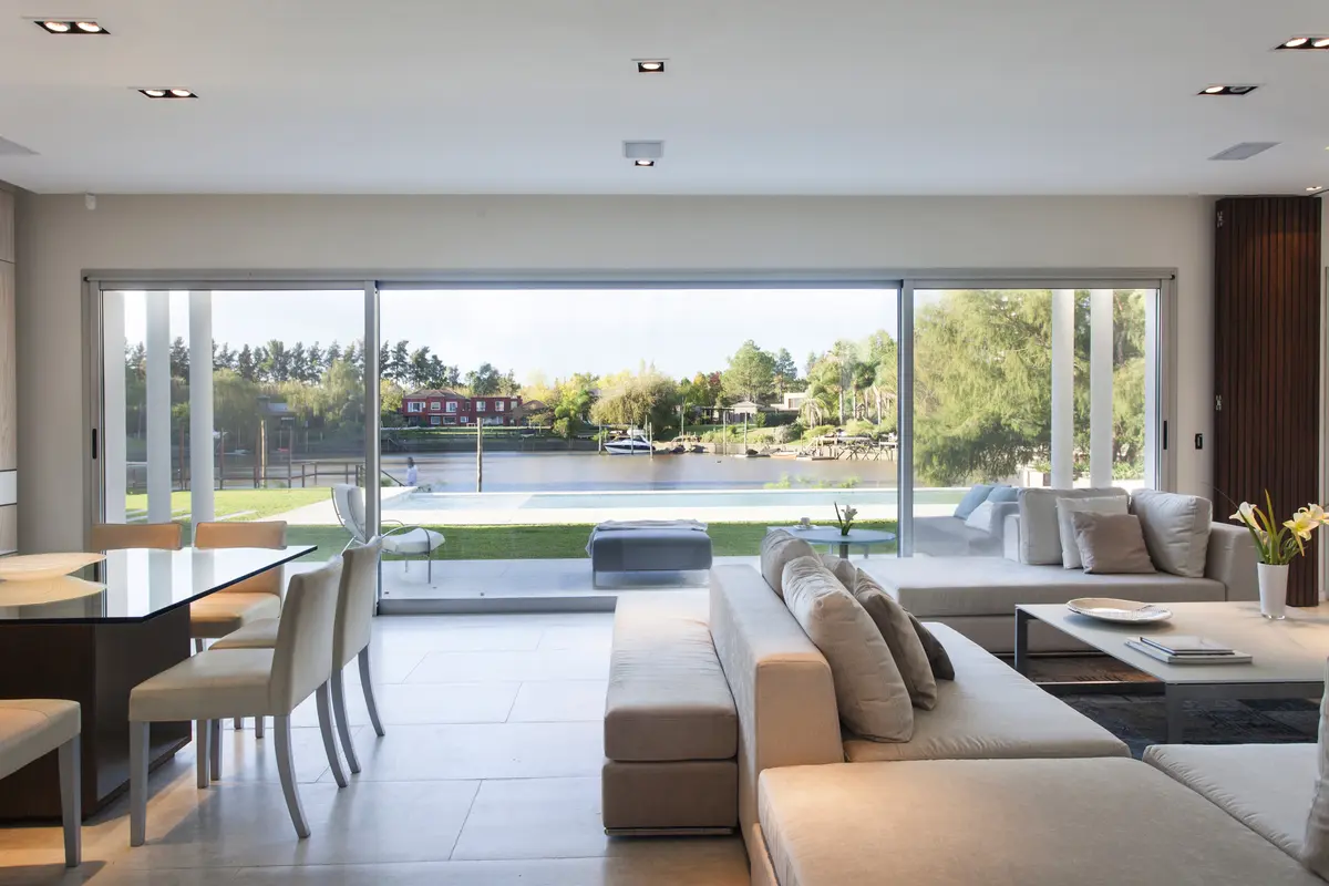 Living moderno con vista al lago y ventanales de piso a techo — proyecto Modernismo Náutico, por Apaarquitectura, en Tigre