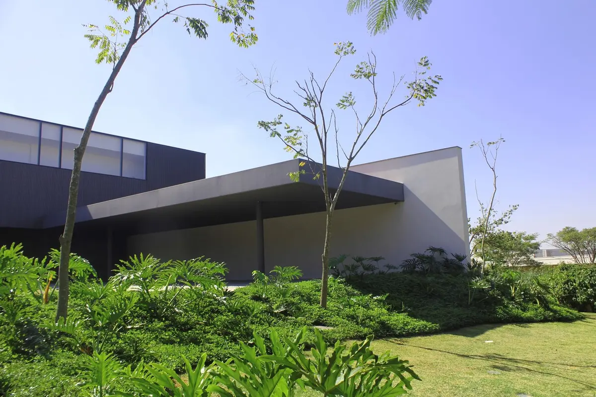 Casa moderna con fachada gris, amplio jardin verde y arboles — proyecto Residência JY, por Gil Fialho