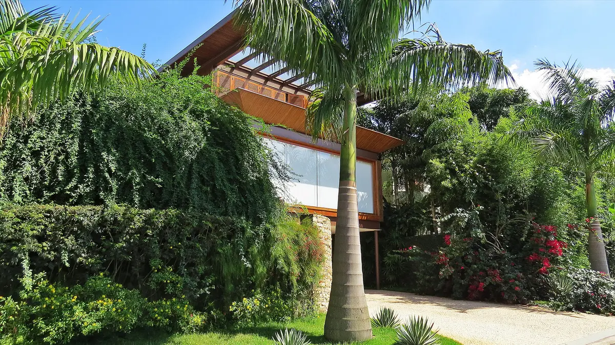 Fachada moderna con pergola, vidrios grandes y jardines frondosos naturales — proyecto Residência MN, por Gil Fialho
