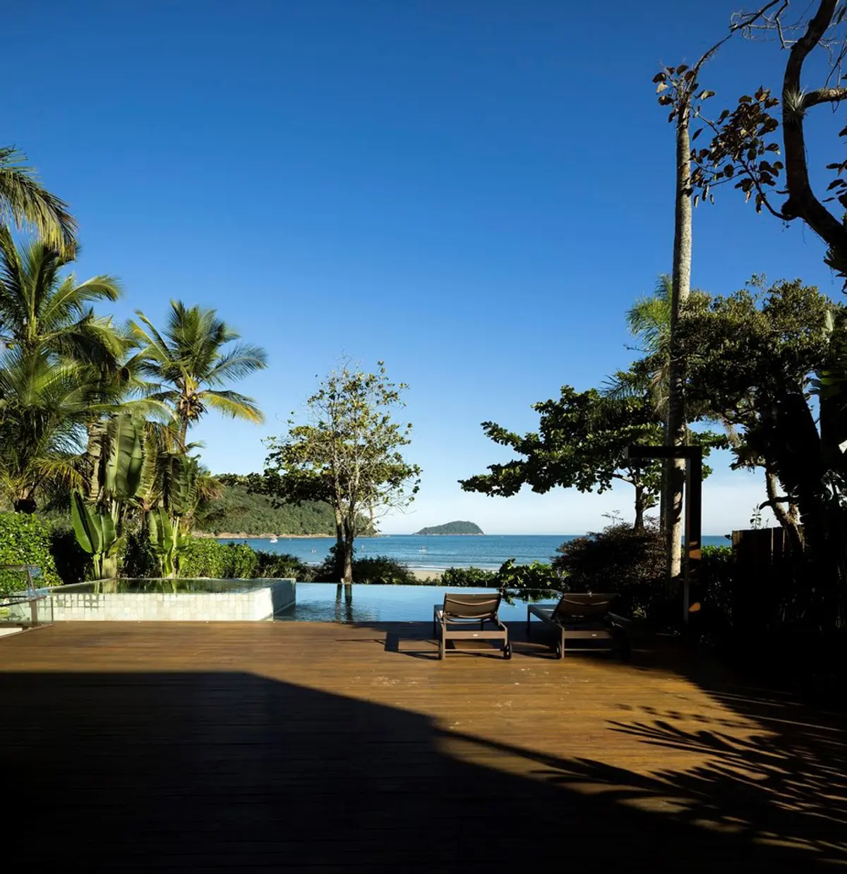 Terraza con deck de madera, pileta y vistas al mar tropical — proyecto West Whales, por Gil Fialho