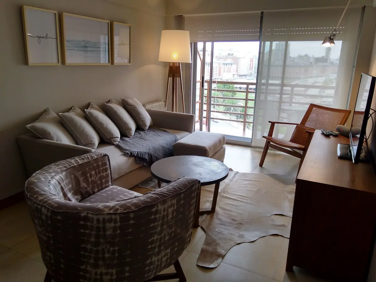 Living moderno con sofá seccional, sillón y ventanales amplios — proyecto Departamento RA, por Vicky Hurrell, en Mar del Plata
